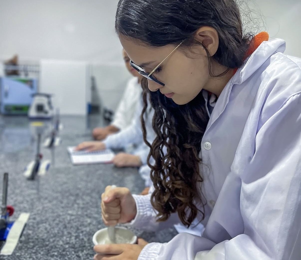 Aluna de jaleco fazendo experimento no laboratório